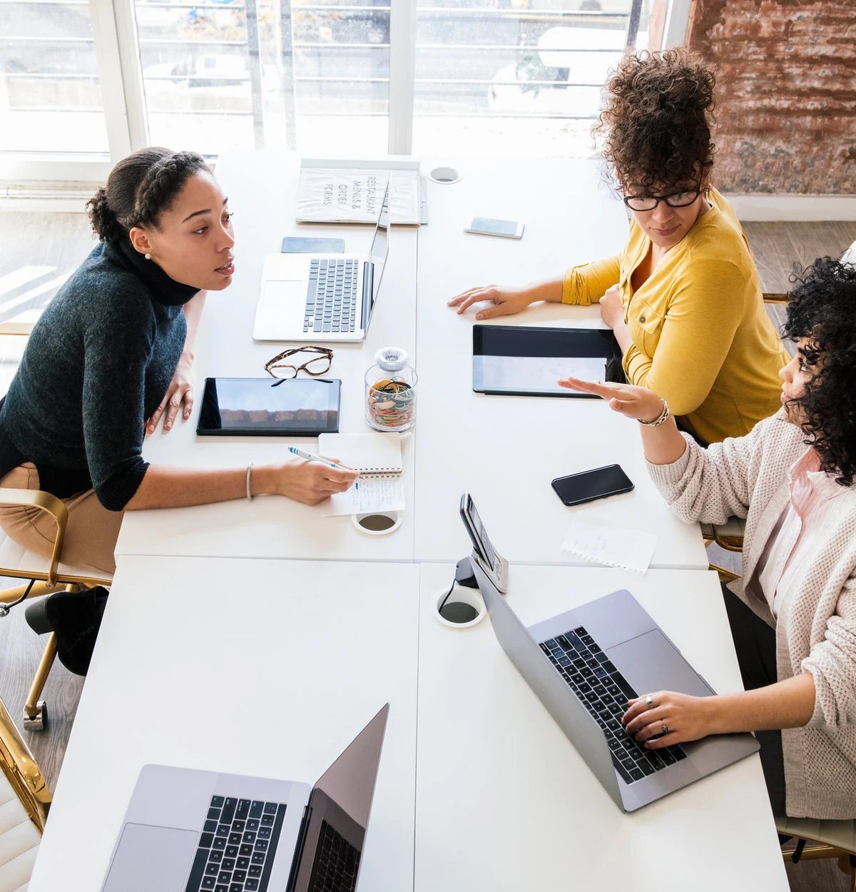 Illustrative scene of three women exchanging ideas around a shared worktable